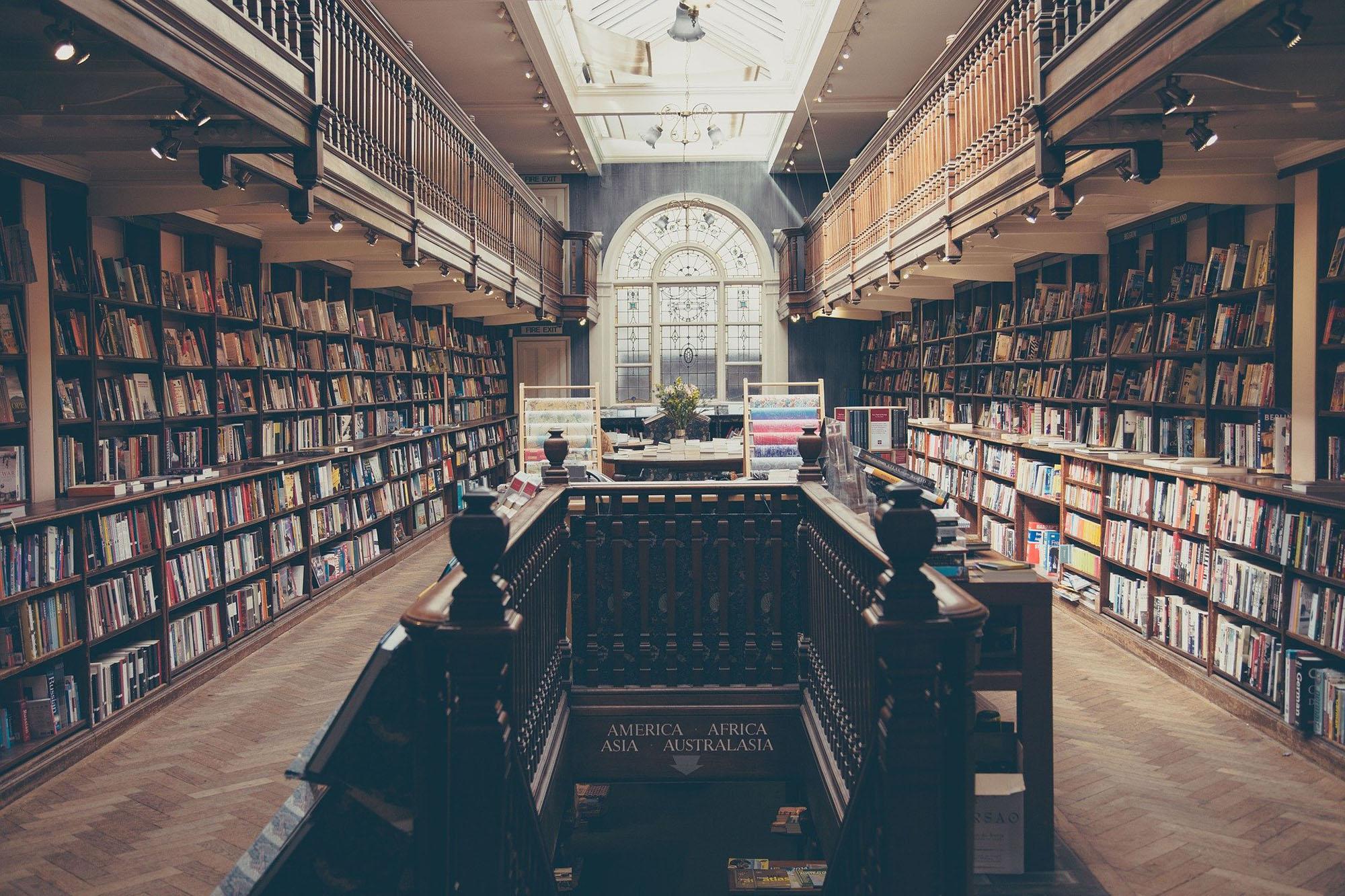 Een bibliotheek met donkere, houten boekenkasten en een houten vloer in visgraatmotief. Op de achtergrond een groot boograam. 